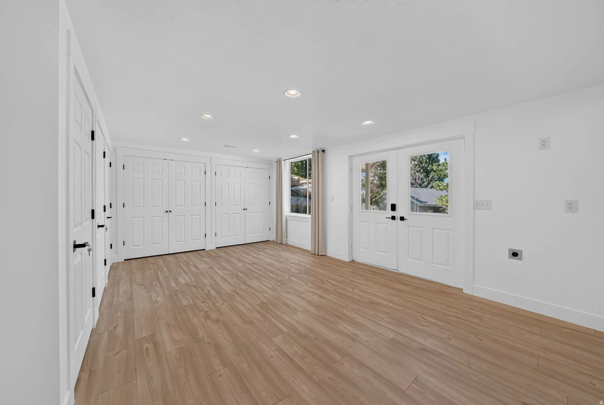 Spacious room featuring light wood-finish flooring, recessed lighting, and white walls