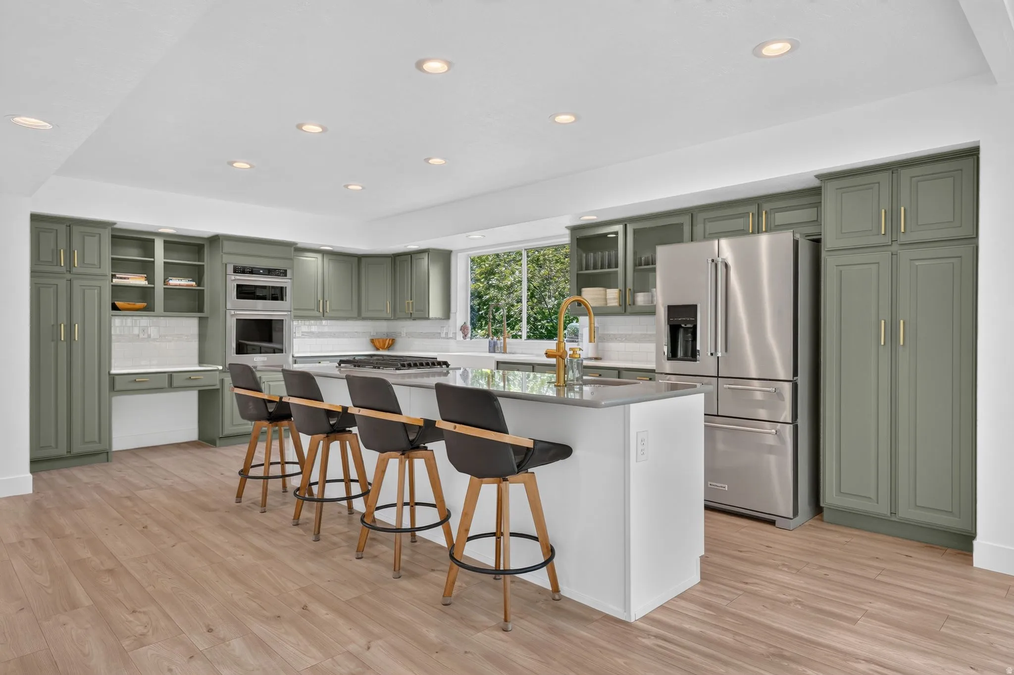 Spacious kitchen featuring sage green cabinetry, stainless steel appliances, a large center island with counter seating, and wood-finish flooring