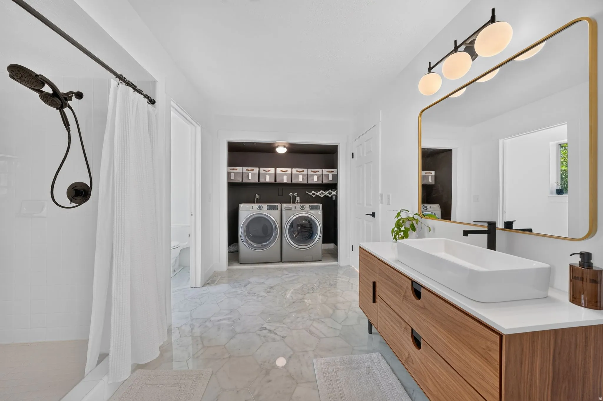 Bathroom featuring a wood-finish vanity with a vessel sink, a gold-framed mirror, and a contemporary four-bulb light fixture