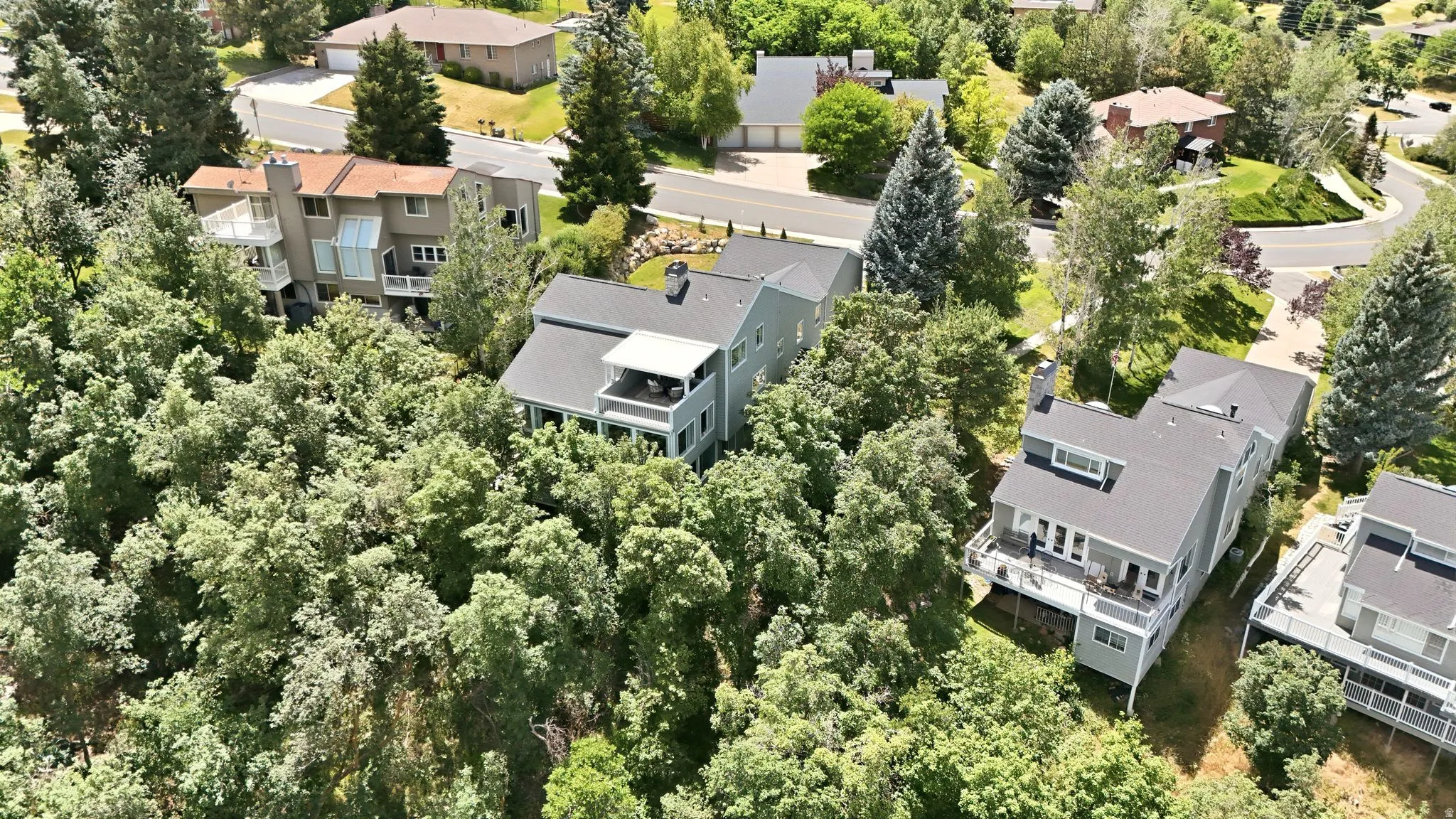 Property featuring multiple balconies, a dark shingle roof, and light-colored siding with heavily wooded privacy