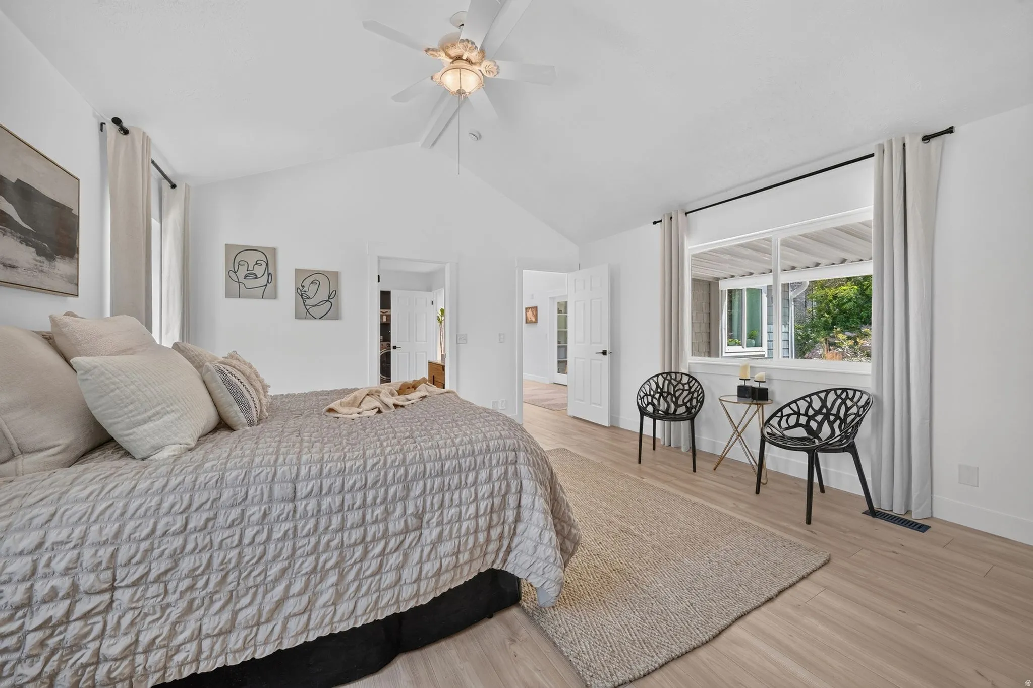 Spacious bedroom featuring vaulted ceilings, a ceiling fan with integrated lighting, wood-finish flooring, and a large window with white trim
