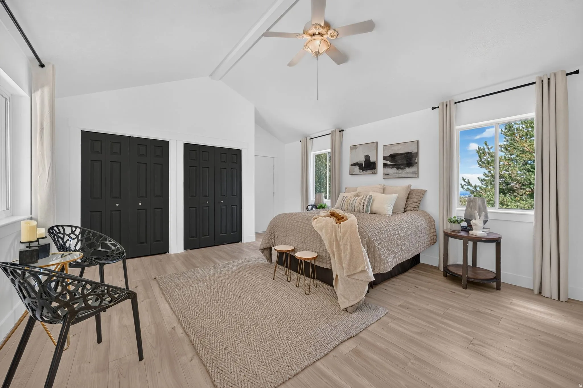 Spacious room featuring vaulted ceilings, light wood-finish flooring, two large windows, and a ceiling fan with integrated lighting
