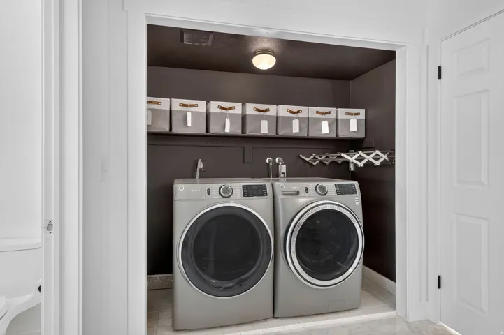 Dedicated laundry area featuring a front-loading washer and dryer, wall-mounted shelving, overhead lighting, and a retractable drying rack