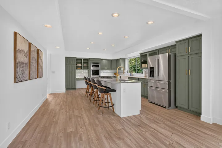 Spacious kitchen featuring sage green cabinetry, stainless steel appliances, a large center island with seating, recessed lighting, and wood-finish flooring