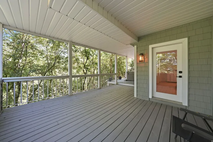 Expansive covered deck featuring wood-finish flooring, white spindle railings, and a full-light glass door