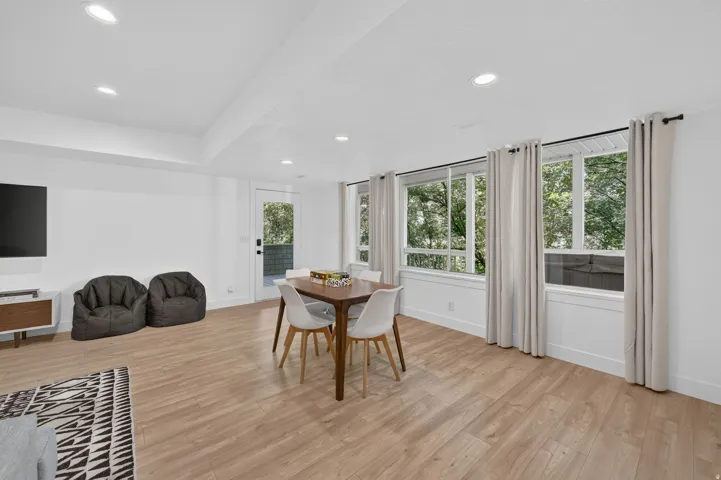 Bright interior space featuring recessed lighting, light wood-finish flooring, multiple windows, a rear exterior door, and white walls