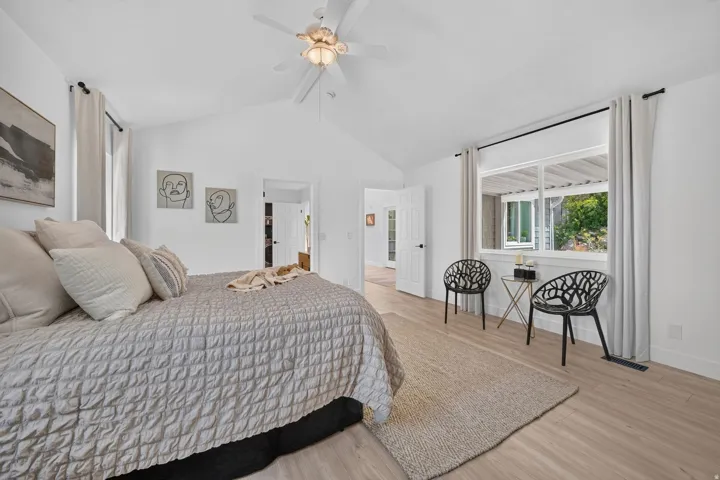 Spacious bedroom featuring vaulted ceilings, a ceiling fan with integrated lighting, wood-finish flooring, and a large window with white trim