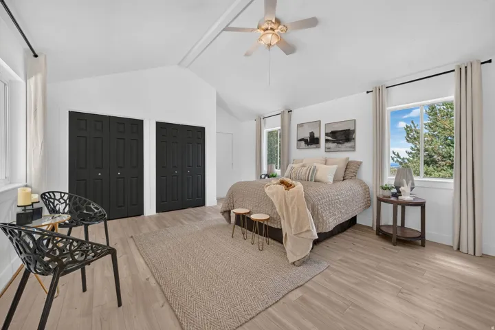 Spacious room featuring vaulted ceilings, light wood-finish flooring, two large windows, and a ceiling fan with integrated lighting