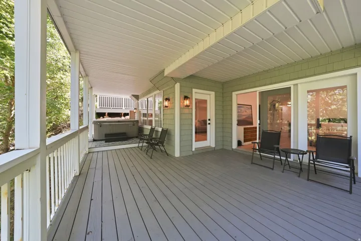 Expansive covered deck featuring wood-finish flooring, a built-in hot tub, and multiple exterior access points