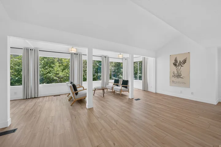Expansive room featuring wood-finish flooring, vaulted ceilings, and a wall of windows