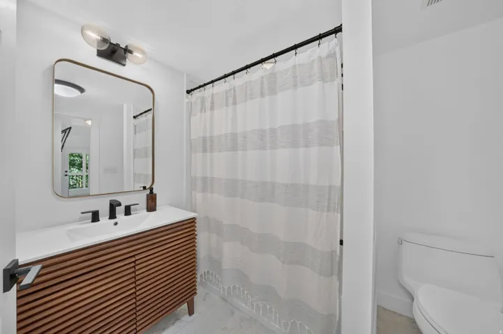 Contemporary bathroom featuring a slatted wood-finish vanity, integrated sink, and matte black fixtures