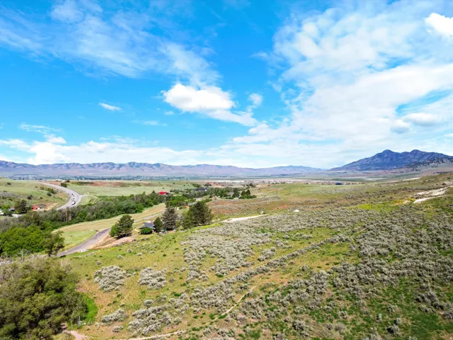 Expansive rural landscape featuring distant mountains, verdant hillsides, scattered trees, and a winding road