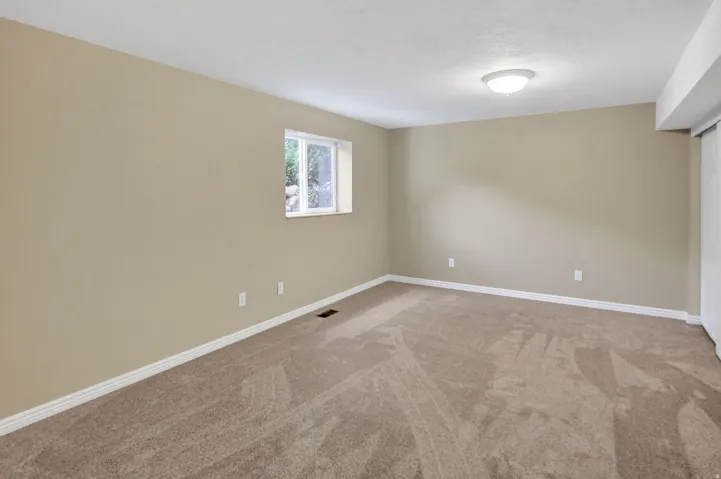 Spacious room featuring neutral carpeting, a single window, and a flush-mount ceiling light fixture