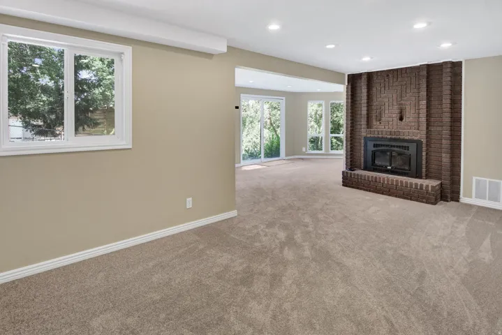 Spacious living area featuring a prominent brick fireplace with hearth, recessed lighting, and neutral carpeting