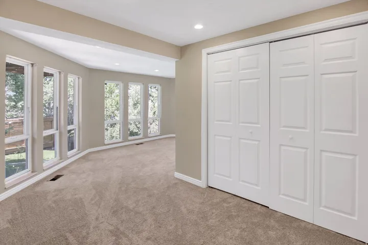Carpeted room featuring multiple tall windows overlooking exterior greenery, closet and sitting area