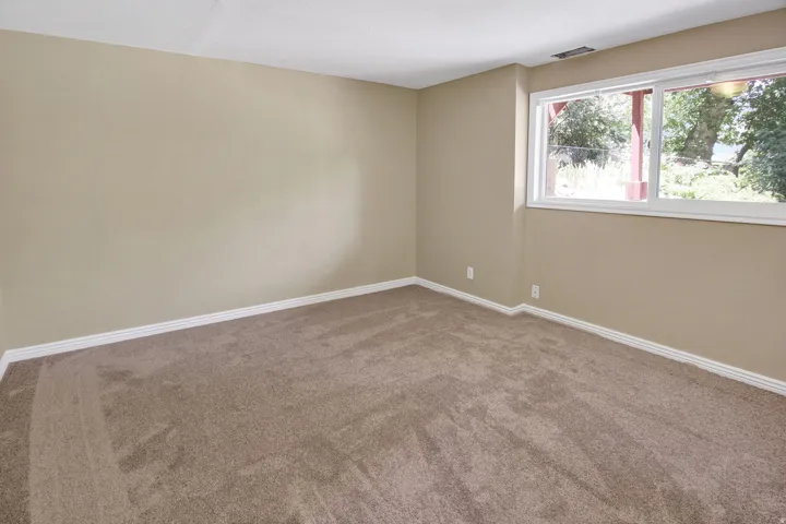Spacious room featuring neutral carpeting, light beige walls, white baseboards, and a large white-framed window