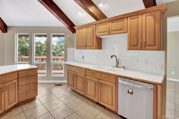 Kitchen featuring natural wood cabinetry with brushed nickel hardware, a white tile backsplash, and light-toned countertops. Newer appliances