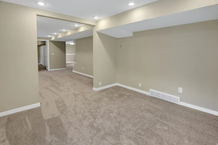 Spacious interior room with neutral-toned carpeting, recessed ceiling lighting, and light beige wall paint Reverse view to bedroom and den office