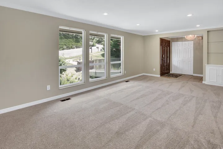 Spacious living area featuring neutral carpeting and light-toned walls, formal entry and built in shelf