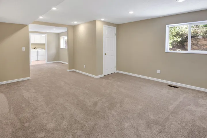 Spacious room with large windows. View to potential kitchen space and laundry