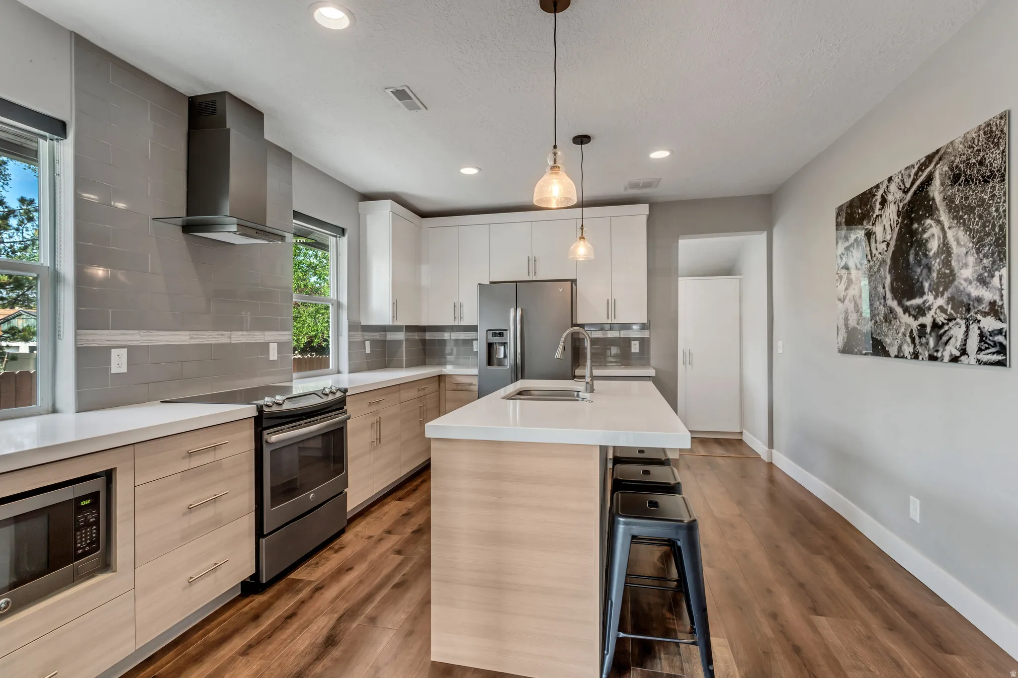 Modern kitchen featuring a central island with bar seating, light-toned wood-finish flooring, white countertops, built-in stainless steel appliances, and sleek upper and lower cabinetry