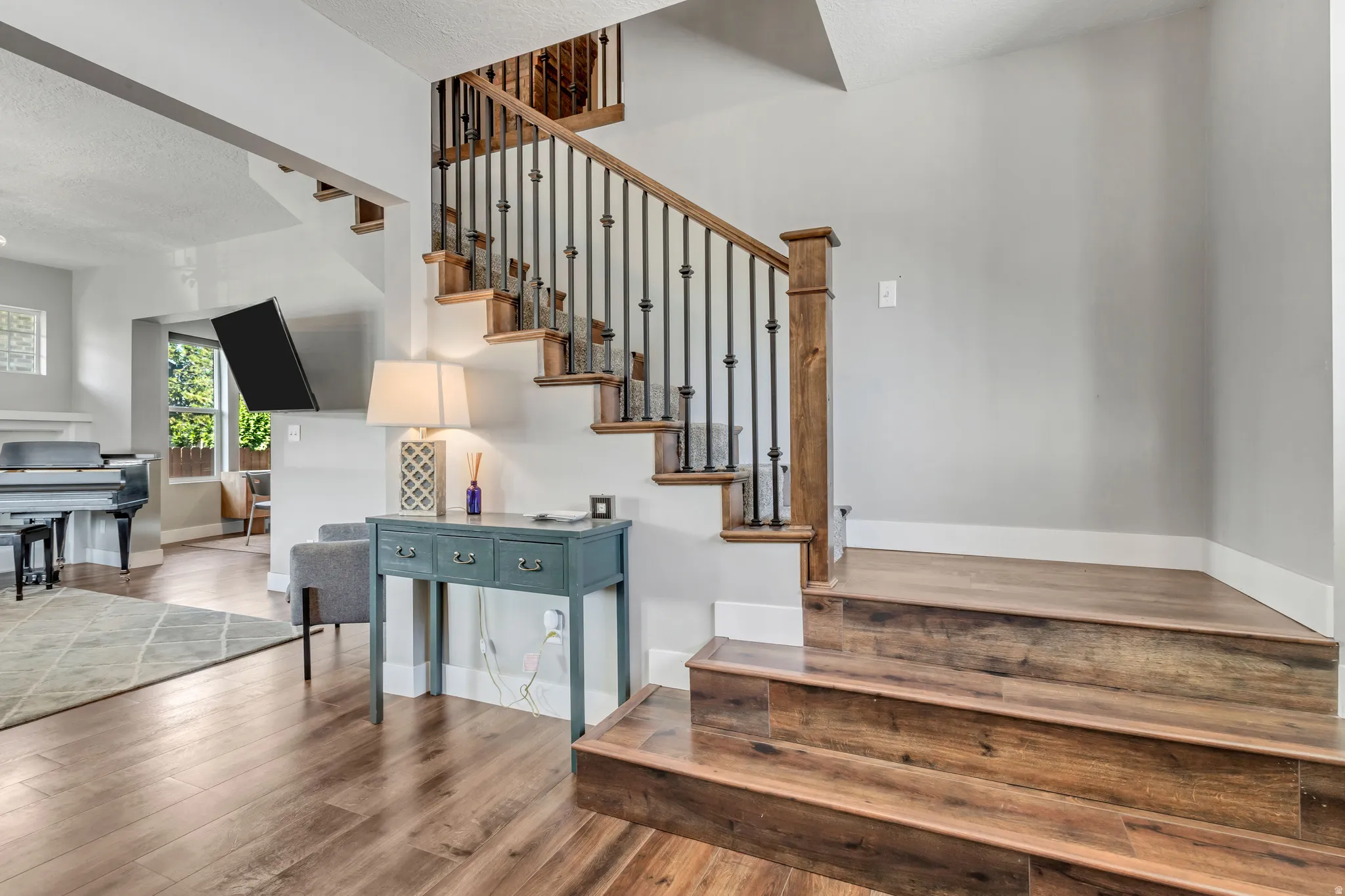 Wood-finish flooring throughout the main level, complemented by a staircase featuring wood treads, wood newel posts, and wrought iron balusters