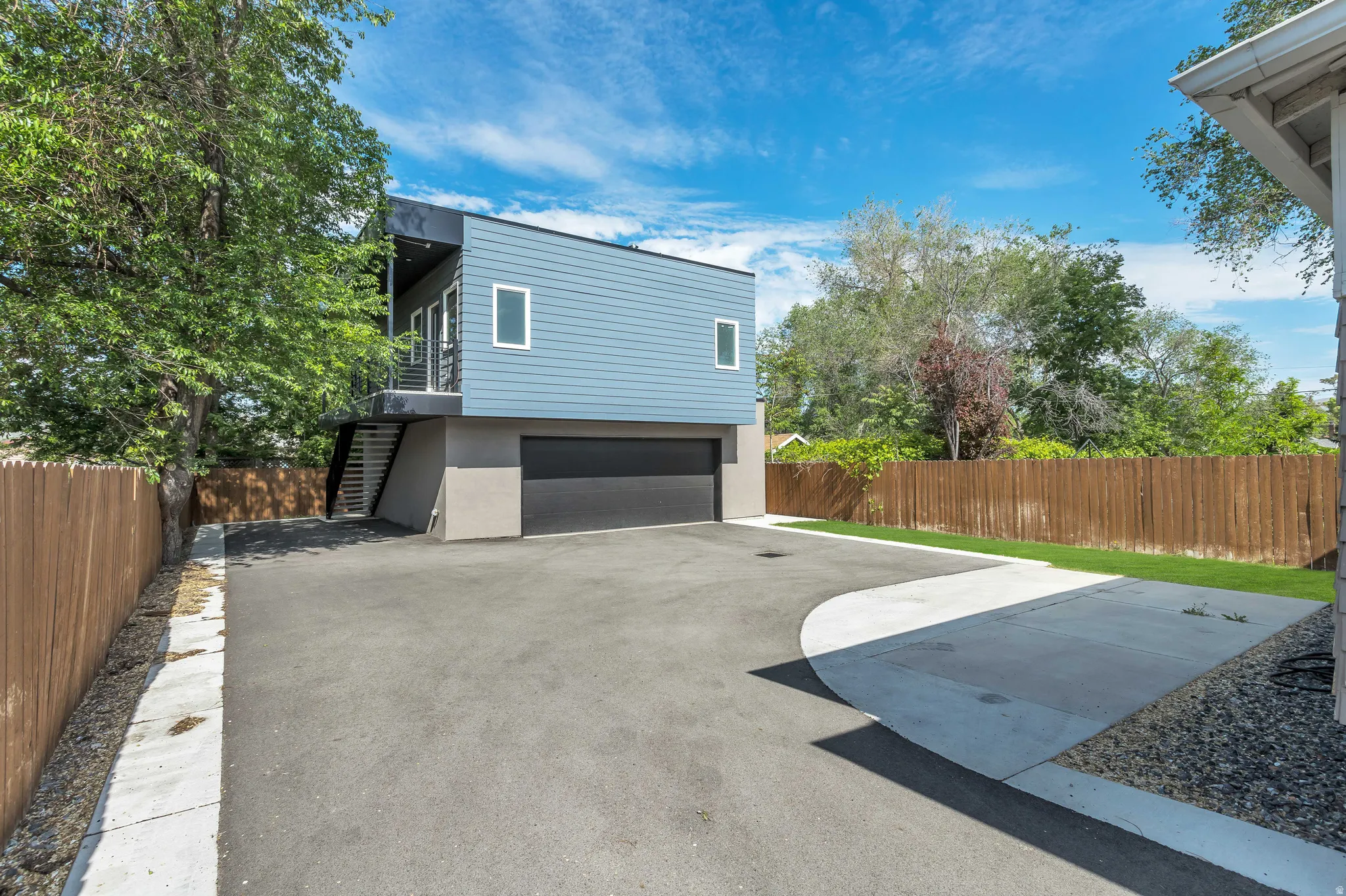 Modern residential structure featuring blue horizontal siding, a black garage door, and a private balcony with metal railings