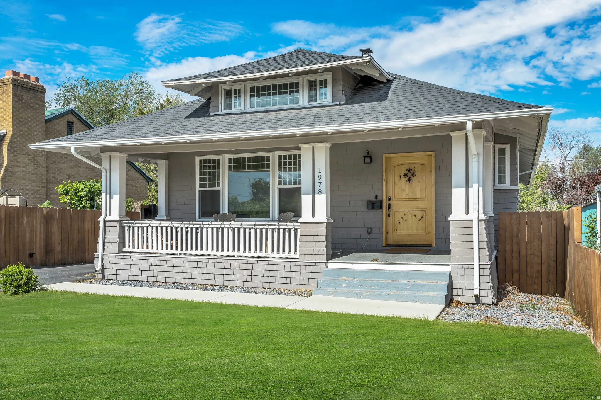 Craftsman-style home featuring gray siding, a covered front porch with white railing, and a distinctive wooden entry door