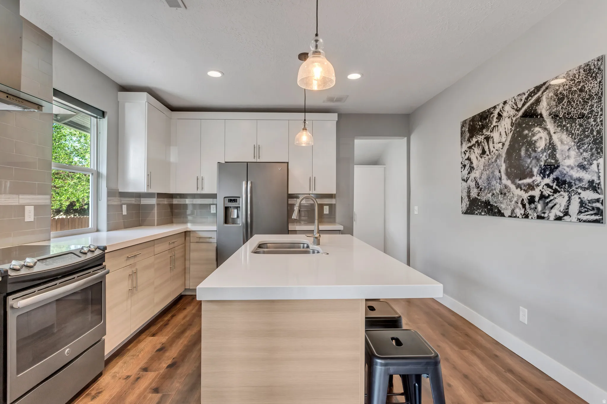 Modern kitchen featuring a large central island with seating, pendant lighting, stainless steel appliances, two-tone cabinetry, and wood-finish flooring