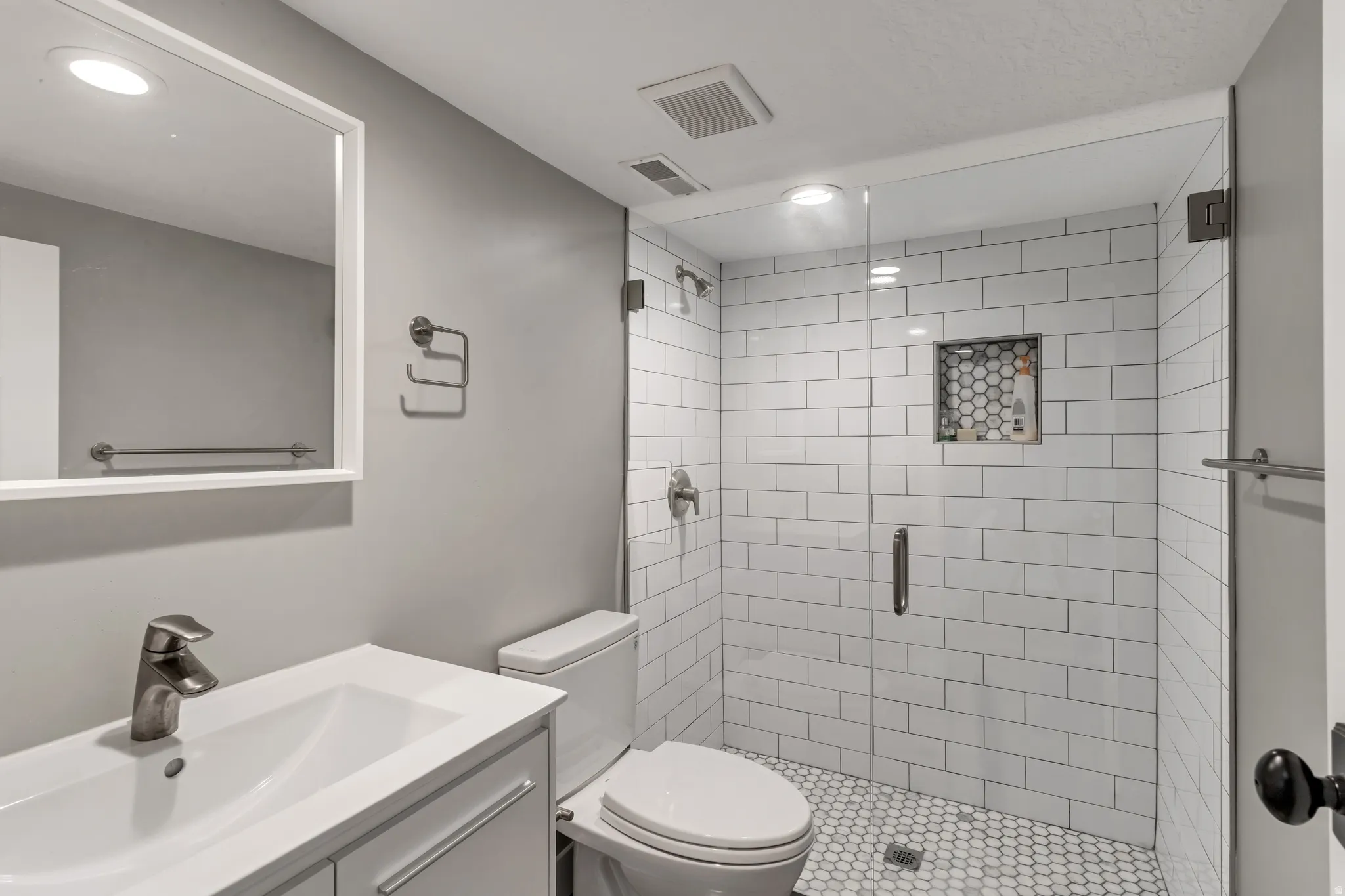 Bathroom featuring a glass-enclosed shower with white subway tile, a hexagonal tile shower niche, and a white hexagonal tile floor
