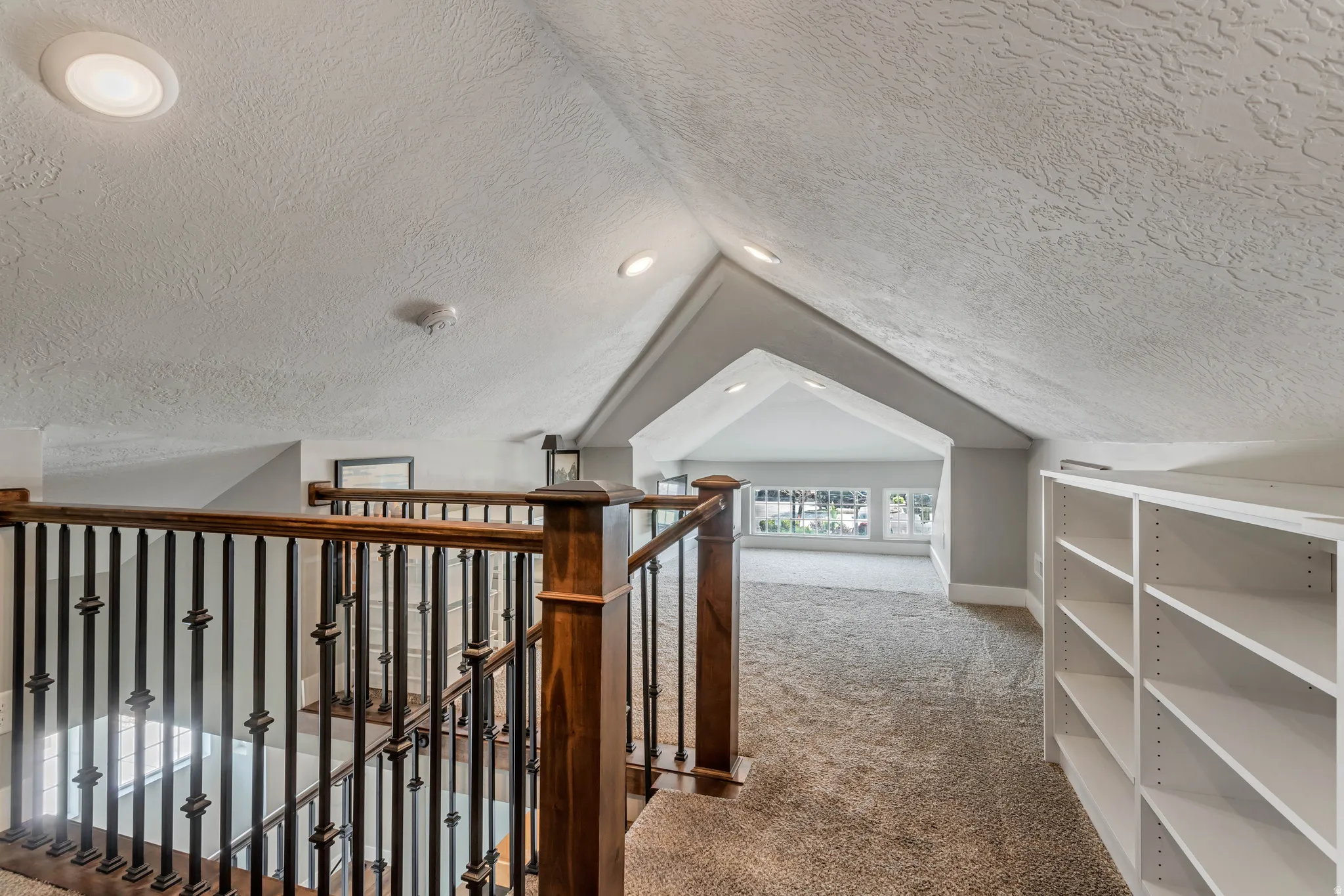 Carpeted upper-level space featuring a vaulted ceiling and built-in shelving