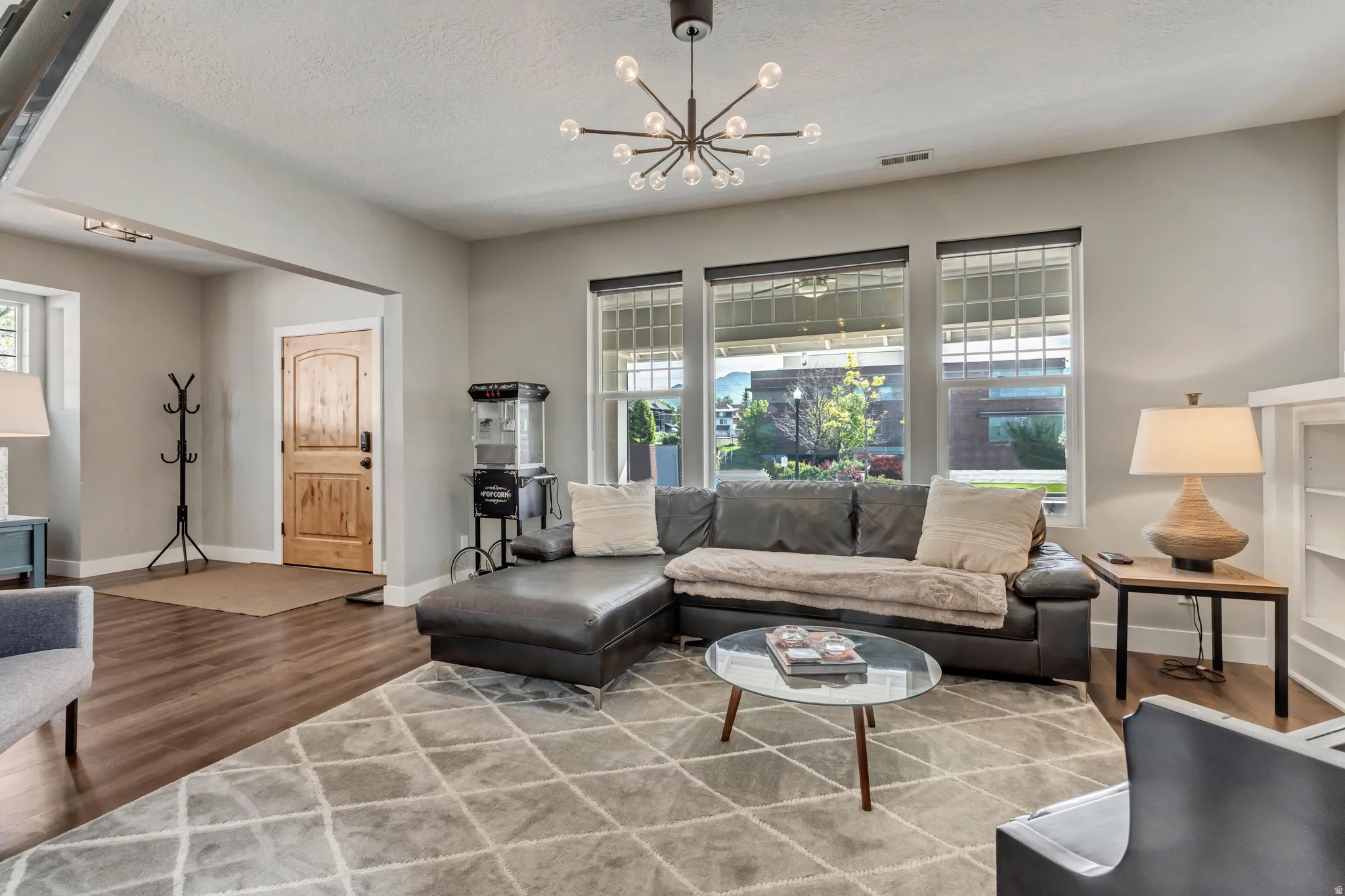 Spacious living area featuring wood-finish flooring, a modern sputnik chandelier, and expansive windows