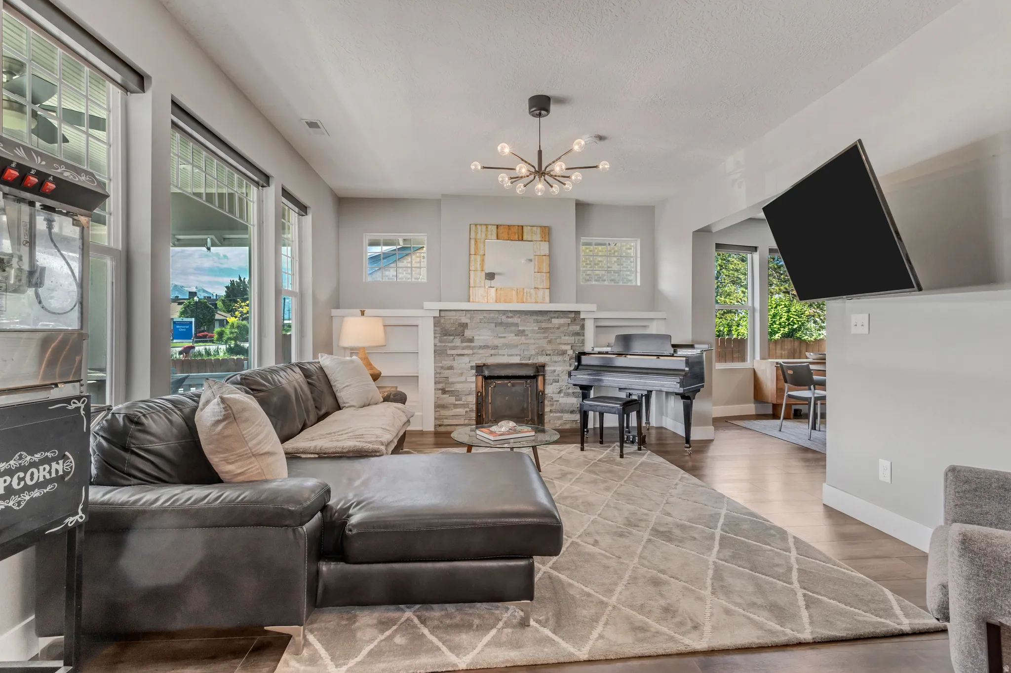Spacious living area featuring wood-finish flooring, a stone-clad fireplace, built-in shelving, expansive windows, and a contemporary chandelier