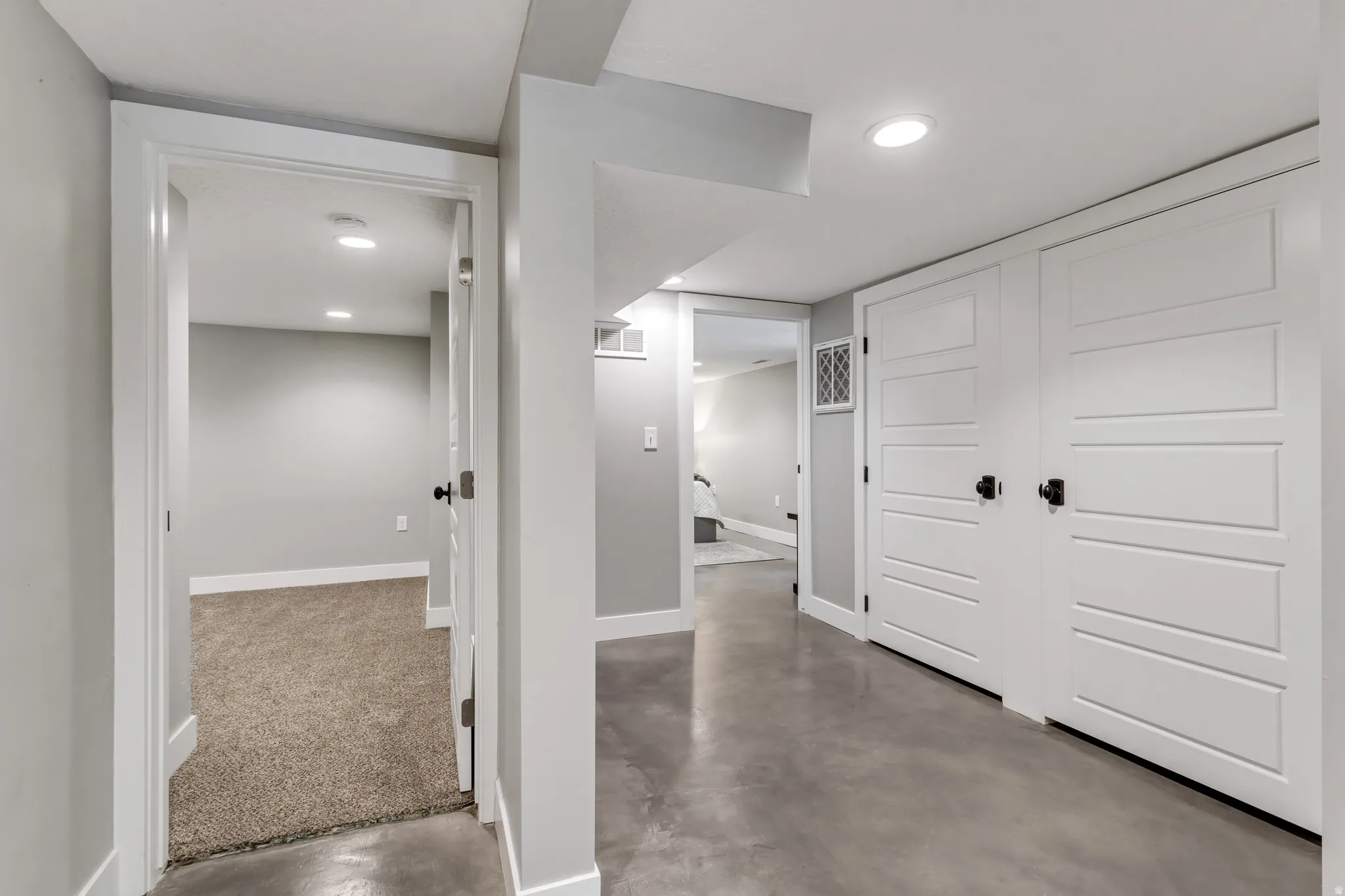 Hallway featuring concrete flooring, recessed lighting, white trim, and multiple white panel doors with black hardware