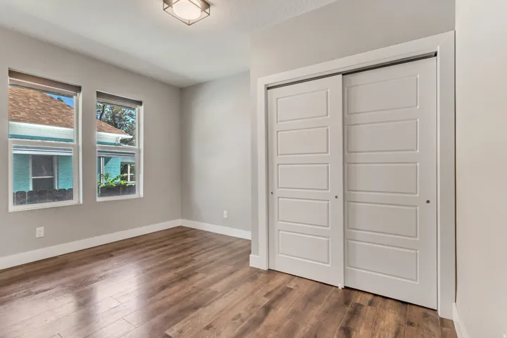 Spacious room featuring wood-finish flooring, two large windows, a flush-mount ceiling light fixture, and a sliding closet with paneled doors