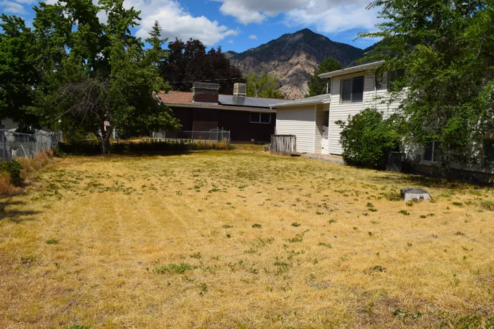 Spacious backyard with a mountain backdrop, mature trees, and a white vinyl-sided exterior