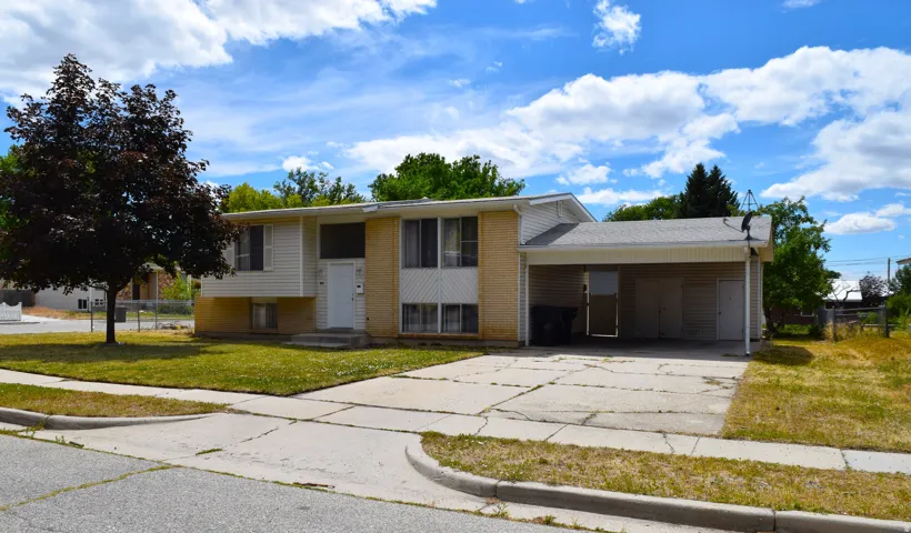 Split-level residence featuring a carport, a paved driveway, and a front lawn with mature trees