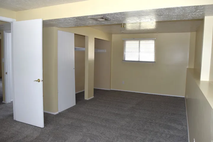 Carpeted interior space featuring a window with blinds, light-toned walls, and recessed storage areas