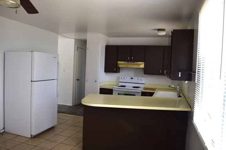 Kitchen featuring dark cabinetry, white appliances, a light-toned countertop, and tile flooring