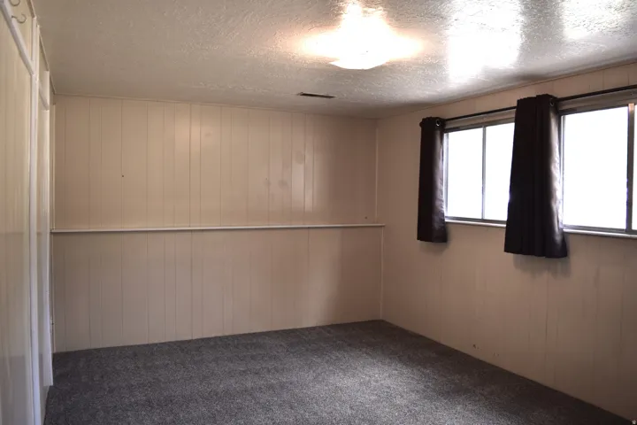 Room with paneled walls, gray carpet, and two multi-pane windows with dark drapery panels
