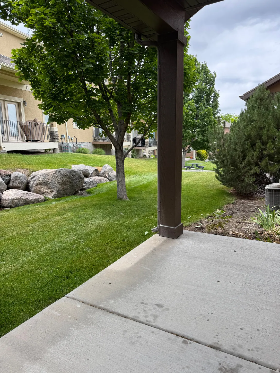 Concrete patio with lush  lawn space, mature trees, and a rock terracing.