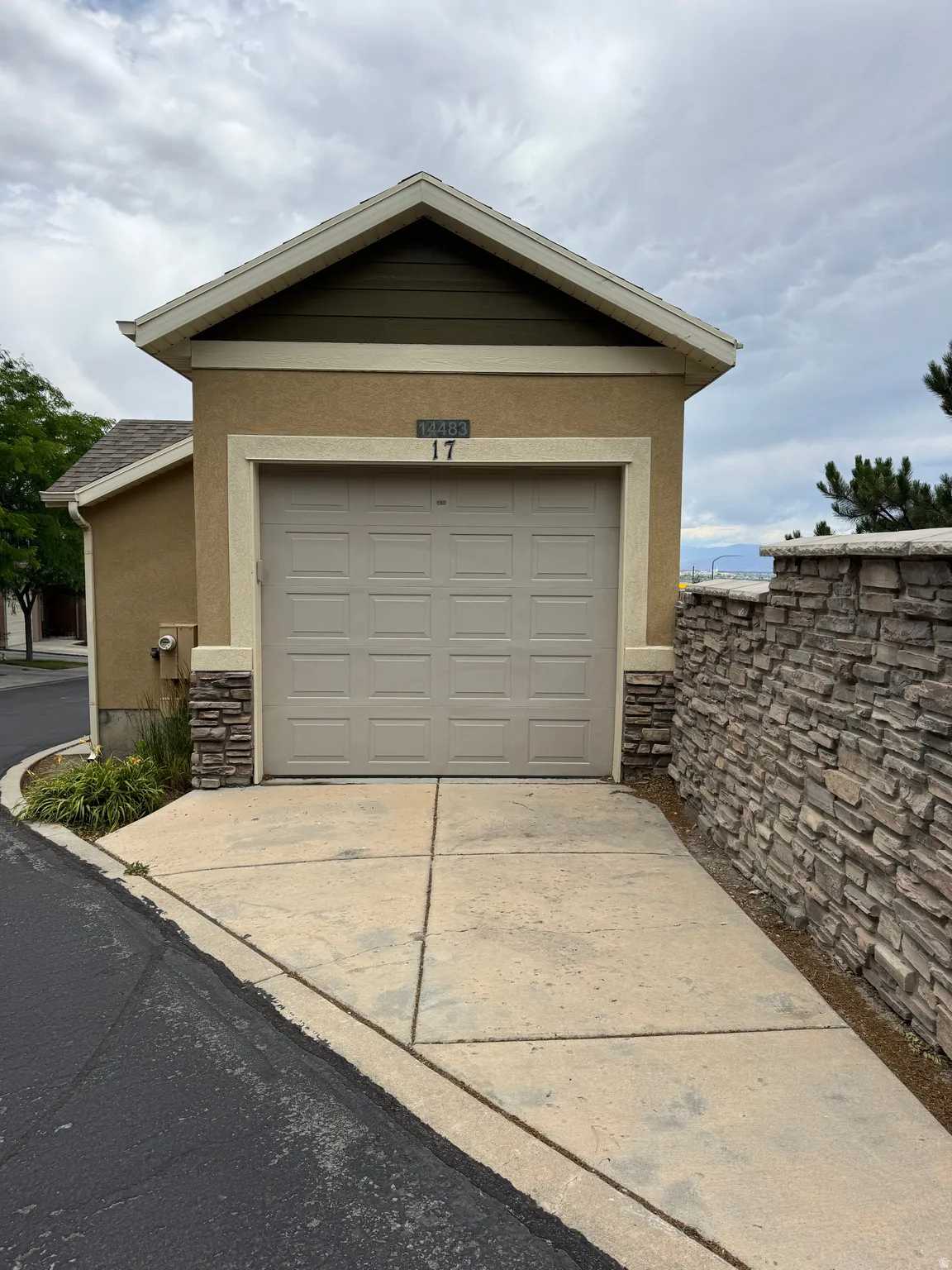 Single-car garage with a paneled door, complemented by a stone veneer accent wall and a gabled roofline featuring green siding