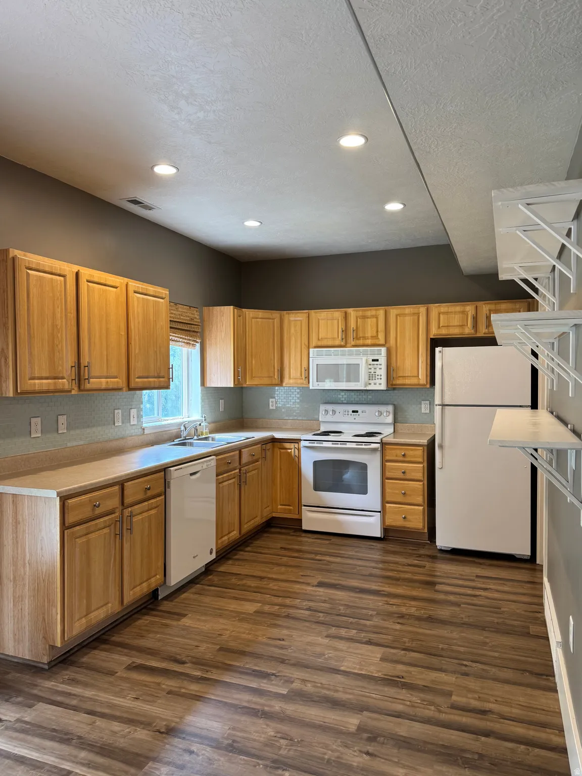 Kitchen features light wood cabinetry and subway tile backsplash, as well as LVP flooring and open shelving for extra storage and display!