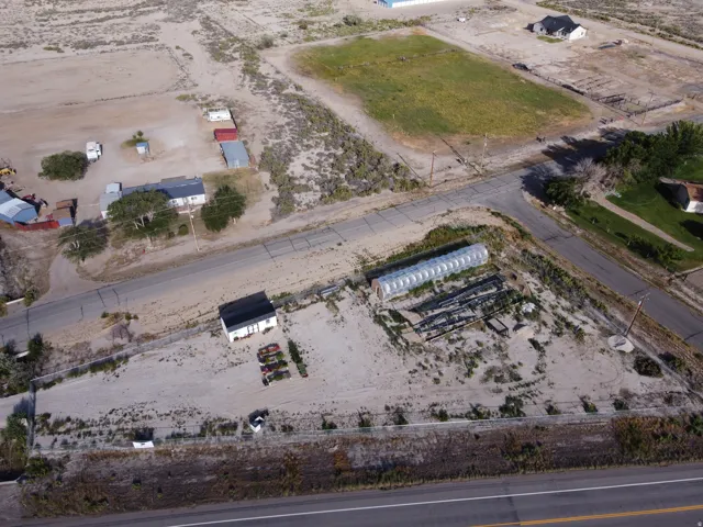 Expansive property featuring a greenhouse structure, a white building with a black roof, and direct road frontage