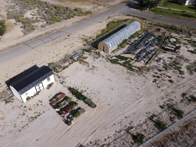 Expansive property featuring a white shed with a black roof, two hoop houses, and organized raised garden beds