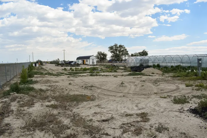 Expansive undeveloped lot featuring a concrete perimeter wall, a standalone structure with white siding and a dark roof, and multiple large hoop houses