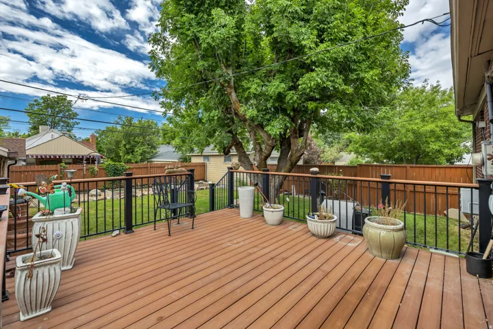 Spacious rear deck featuring wood-finish decking, black metal railings with wood-finish top rails, and a large mature tree providing natural coverage