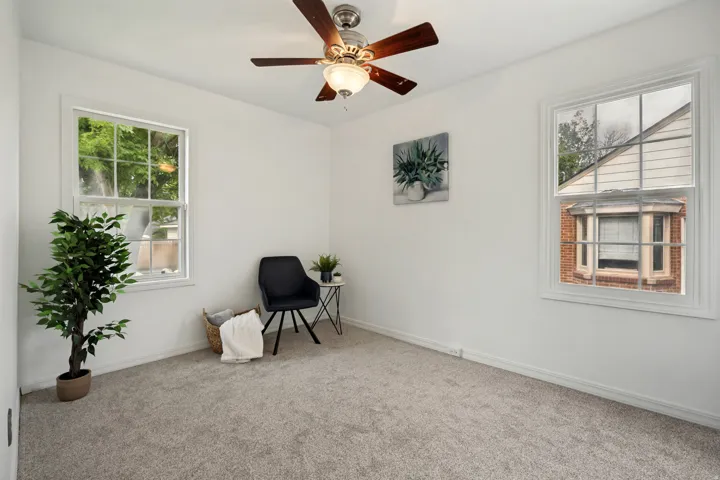 Bright room featuring two large windows, neutral-toned carpeting, and a ceiling fan with light fixture