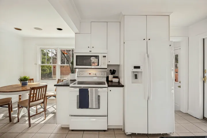 Bright kitchen featuring white cabinetry, a white appliance suite, dark countertops, and tile flooring