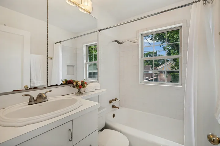 Bathroom featuring a window above the tub, white subway tile surround, white vanity with integrated sink, and an expansive mirror